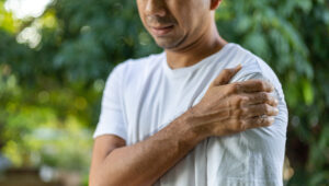 Man in white T-shirt gripping his painful frozen shoulder