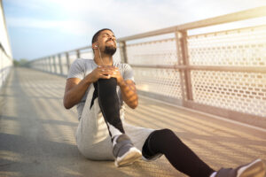 Athletic man sitting on running path clutching his painful knee