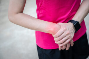 Close up of athletic woman in pink shirt holding her sprained wrist