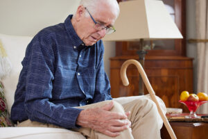 Older man sitting on couch with cane by his side holding his arthritis knee