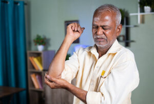 Older man wearing yellow shirt holding his arthritic elbow