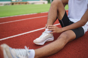 Male runner sitting on track holding his painful ankle